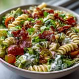 Creamy BLT Pasta Salad with Bacon and Avocado in a white bowl, topped with crisp bacon bits and fresh herbs.  