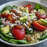 Colorful quinoa salad featuring ripe strawberries, diced avocado, and fresh spinach, topped with toasted almonds and a zesty lemon-honey vinaigrette.  