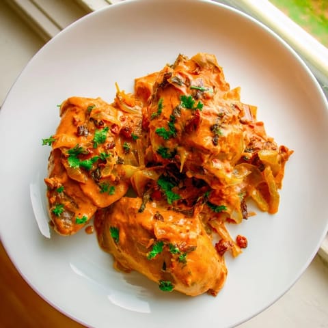 A hearty bowl of Chicken Tikka Masala, speckled with cilantro, served alongside fluffy white rice.