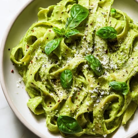 A fork lifts a bite of Creamy Green Pea Alfredo, revealing silky fettuccine coated in a luscious sauce with a garnish of grated Parmesan.