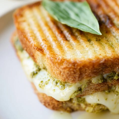 Caprese Pesto Grilled Cheese, sliced diagonally to reveal layers of gooey cheese, juicy tomatoes, and aromatic basil pesto spread.  