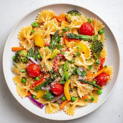 Brightly colored Rainbow Veggie Pasta Primavera in a white bowl, showcasing bow-tie pasta mixed with asparagus, cherry tomatoes, and red bell peppers.  