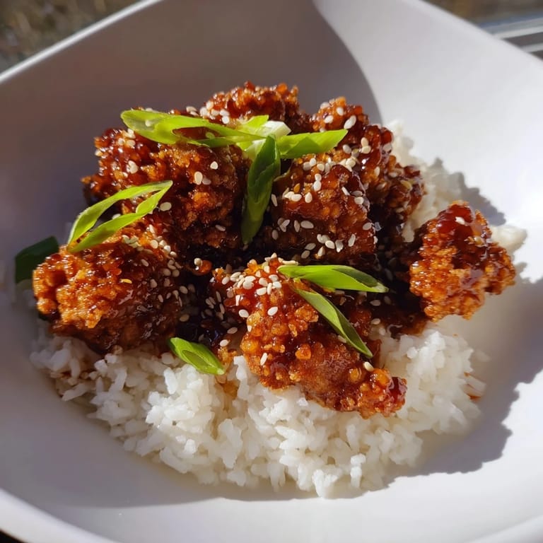A steaming plate of General Tsos Chicken: sweet and spicy chicken served with garnished rice.