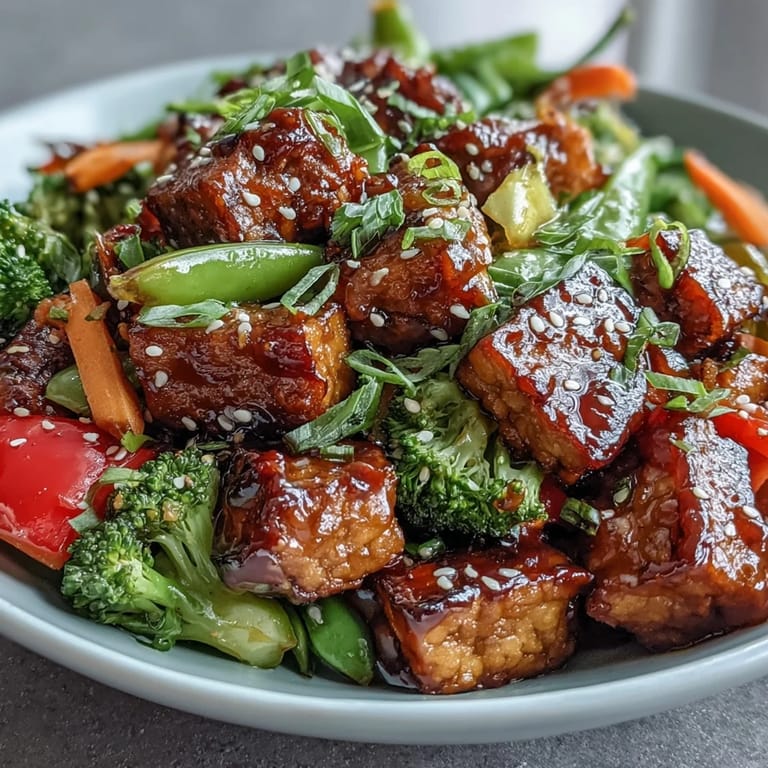 Steaming bowl of vegetable tempeh stir-fry garnished with sesame seeds and fresh cilantro, served over white rice.