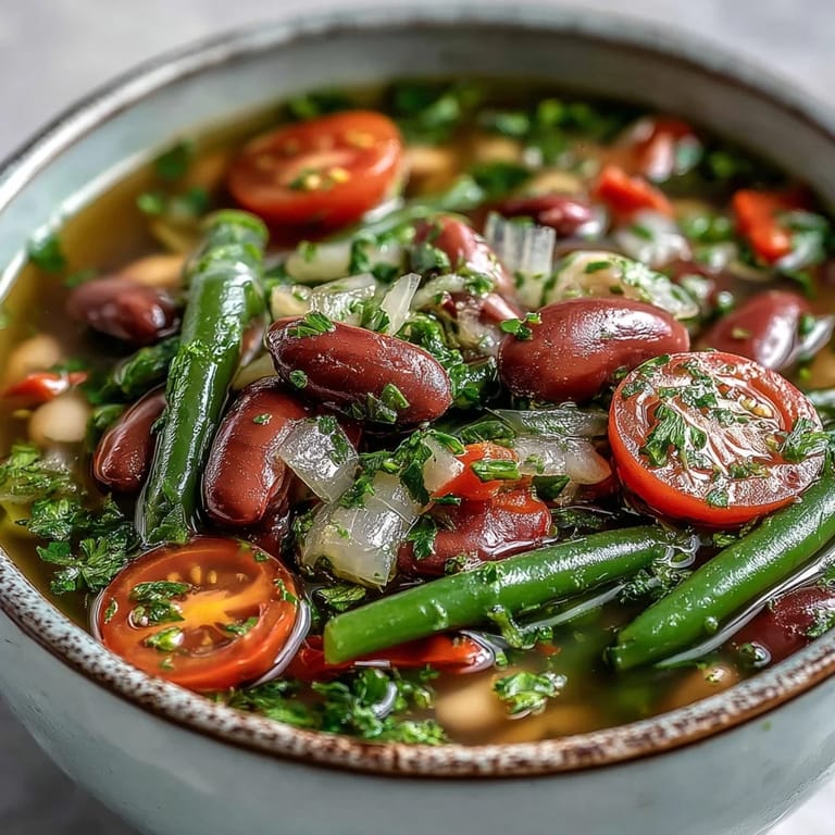 Close-up of Three-Bean Salad Soup, revealing glossy beans and fresh herbs floating in a rich, steamy broth, ready to serve with crusty bread.