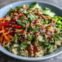A vibrant Thai Coconut Quinoa Bowl topped with crisp carrots, red bell peppers, and creamy peanut dressing.  