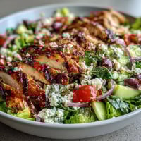 A vibrant Greek salad bowl topped with juicy grilled chicken, fresh vegetables, and tangy feta cheese.  