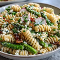 Spring pasta salad with lemon vinaigrette and radishes, vibrant and fresh, served in a white bowl with crisp vegetables and tender pasta.